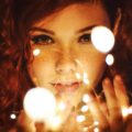 Enchanting close-up of a woman with red hair and freckles surrounded by glowing fairy lights.